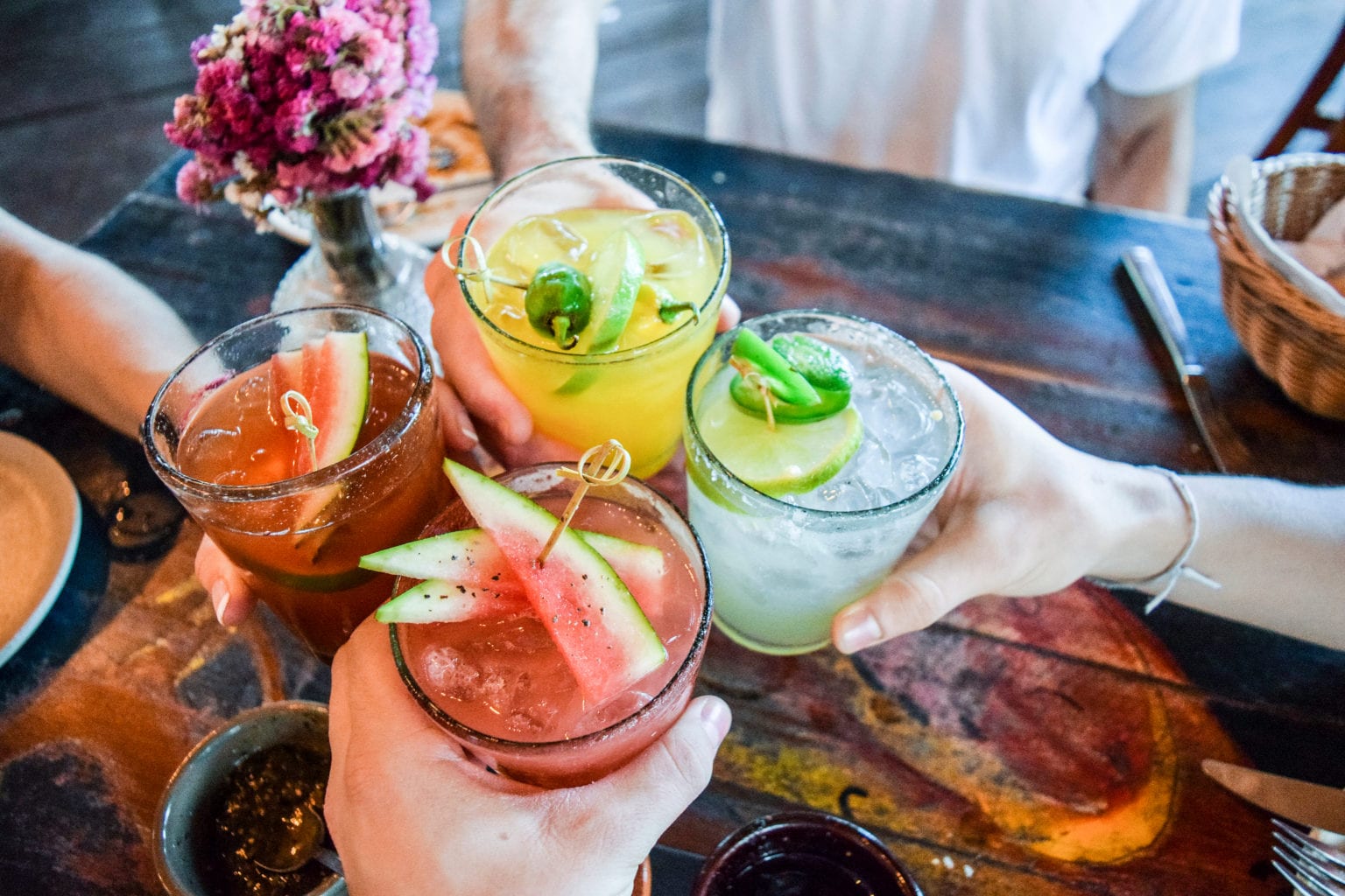 photo of four arms holding different fancy cocktails together while they cheers