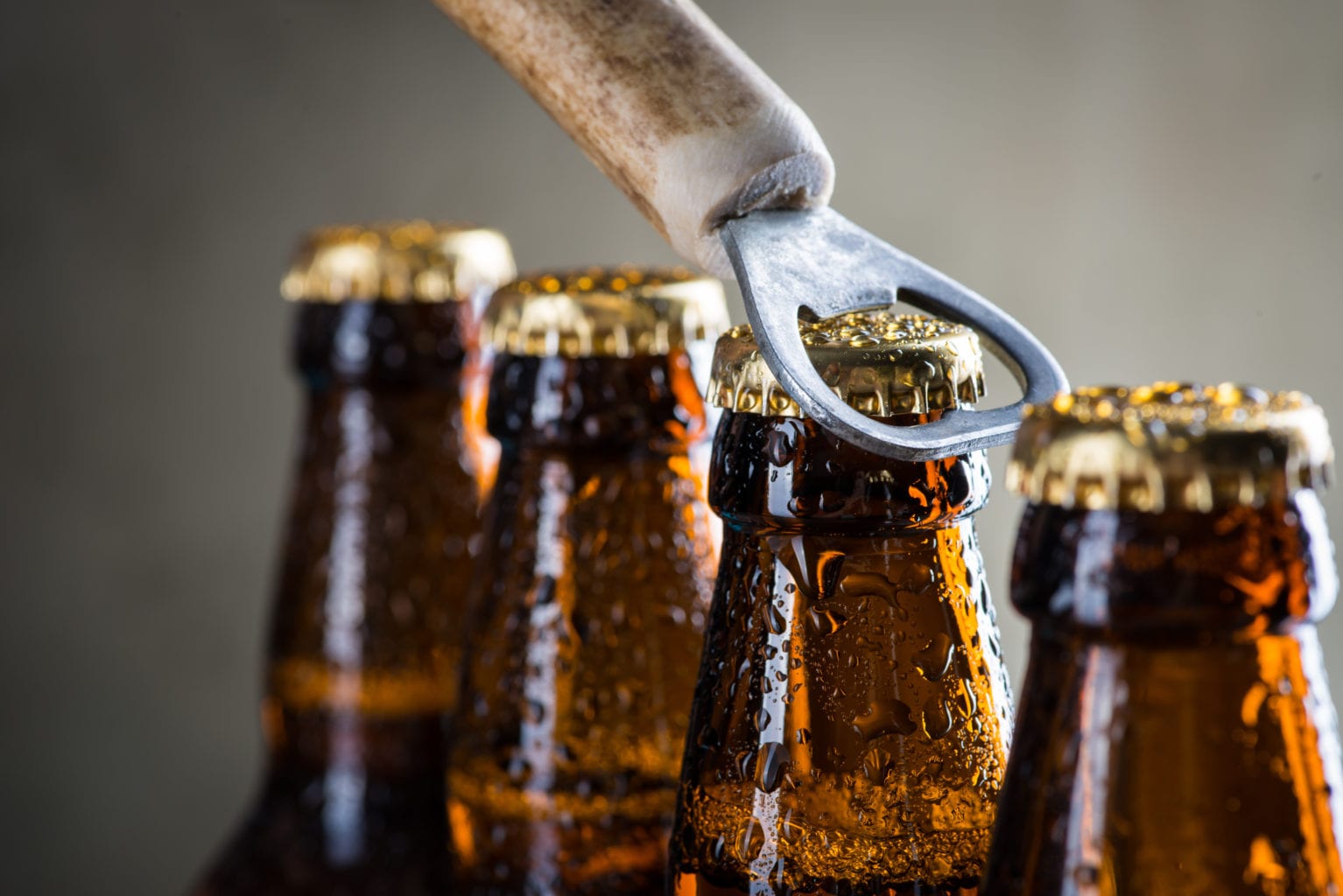 photo of a row of brown beer bottles with an opener about to pop the top on one beer