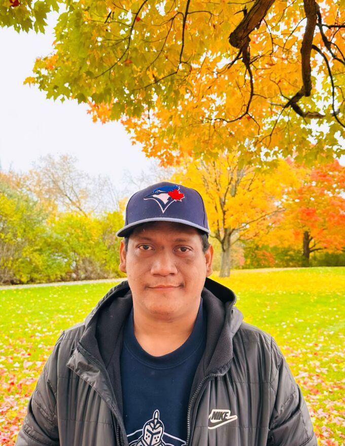 photo of Hubert Magos in a park in autumn, under a tree with orange and green leaves that are falling